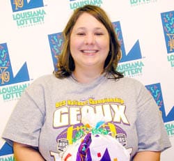 Woman in a gray football tshirt holds a Louisiana Lottery prize bag and smiles in front of a white background patterned with the Louisiana Lottery logo