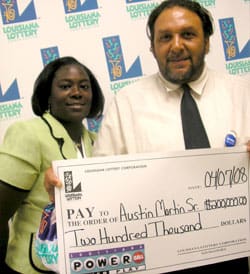 Man and woman smile with oversized check in front of a white background patterned with the Louisiana Lottery logo