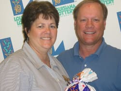 Man and woman smile together in front of a white background patterned with the Louisiana Lottery logo
