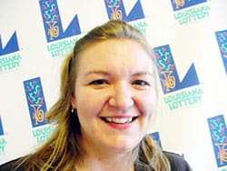 Woman with blonde hair smiles in front of a white background patterned with the Louisiana Lottery logo