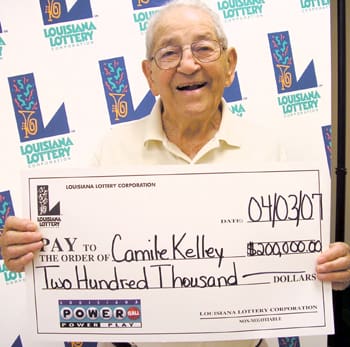 Older man smiles with oversized check in front of a white background patterned with the Louisiana Lottery logo