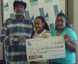 Man, woman, and young girl smile with oversized check in front of a white background patterned with the Louisiana Lottery logo