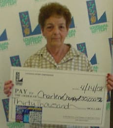 Woman with short curly hair and a green checked shirt holds a giant check in front of a white background patterned with the Louisiana Lottery logo