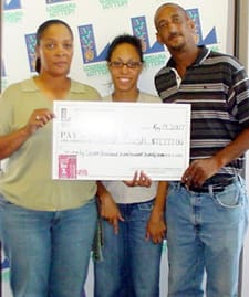 Two women and a man smile with an oversized check in front of a white background patterned with the Louisiana Lottery logo