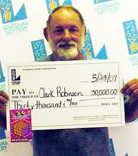 Bearded older man holds oversized white check in front of a faded white backdrop printed with the Louisiana Lottery logo