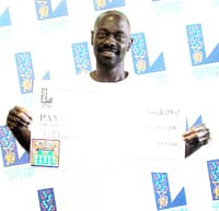 Man holds oversized check in overexposed photo in front of a white background patterned with the Louisiana Lottery logo