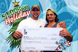 Two men in baseball caps smile with an oversized check in front of a blue digital background with a cartoon Christmas tree and the words "$100,000 Holiday!"