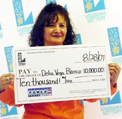 Curly haired woman in an orange shirt smiles with a giant check in front of a faded white background patterned with the Louisiana Lottery logo
