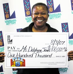 Woman beams with a giant check in front of a white background patterned with the Louisiana Lottery logo
