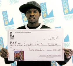 Man in a baseball hat holds an oversized check in front of a faded white background patterned with the Louisiana Lottery logo