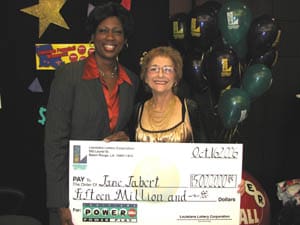 Two women pose with giant check in front of a dark background decorated with balloons and stars