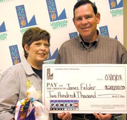 Man and woman hold oversized check and a Louisiana Lottery prize bag in front of a white background patterned with the Louisiana Lottery logo