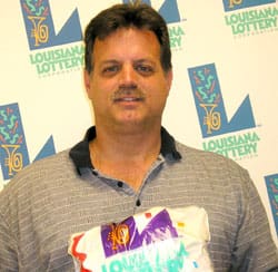 Man in gray striped collared shirt holds Louisiana Lottery branded prize bag in front of a white background patterned with the Louisiana Lottery logo