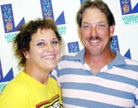 Man and woman smile together in front of a white background patterned with the Louisiana Lottery logo