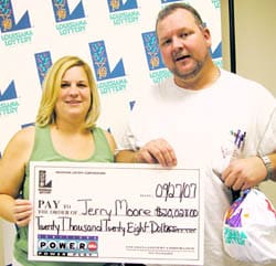 Man and woman pose with giant check in front of a white background patterned with the Louisiana Lottery logo