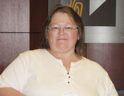 Woman in a white buttoned shirt and glasses smiles in a Louisiana Lottery office