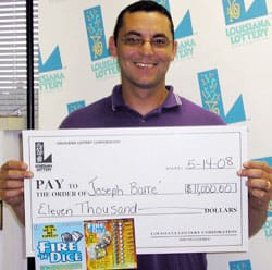Man in a purple polo and glasses holds a giant check in front of a white background patterned with the Louisiana Lottery logo