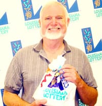 Older man smiles with Louisiana Lottery prize bag in front of a white background patterned with the Louisiana Lottery logo