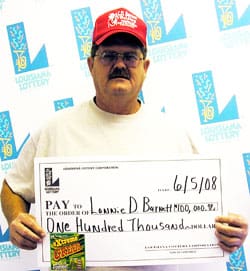 Man in red cap and white tshirt poses with oversized check in front of a white background patterned with the Louisiana Lottery logo