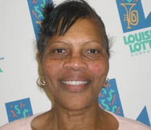 Woman with a pink top smiles in front of a white background patterned with the Louisiana Lottery logo