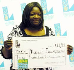 Woman in a white and black floral top holds an oversized check in front of a faded white background patterned with the Louisiana Lottery logo