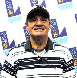 Man in a black and white striped polo and a white cap smiles in front of a white background patterned with the Louisiana Lottery logo