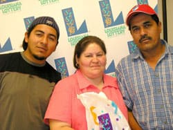 Two men and a woman hold a Louisiana Lottery prize bag in front of a white background patterned with the Louisiana Lottery logo