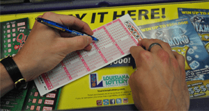 Person using a pen to fill out a Powerball game slip on a counter covered in Louisiana Lottery advertisements