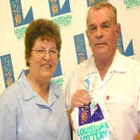 Man and woman hold a Louisiana Lottery prize bag in front of a white background patterned with the Louisiana Lottery logo