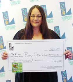 Long haired woman with glasses smiles with oversized check in front of a white background patterned with the Louisiana Lottery logo