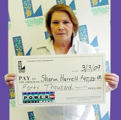 Woman holds an oversized check in front of a white background patterned with the Louisiana Lottery logo