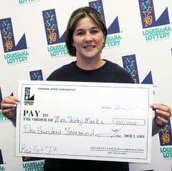 Woman in a black tshirt poses with oversized check in front of a white background patterned with the Louisiana Lottery logo