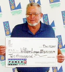 Man in a blue collared shirt holds an oversized check in front of a white background patterned with the Louisiana Lottery logo