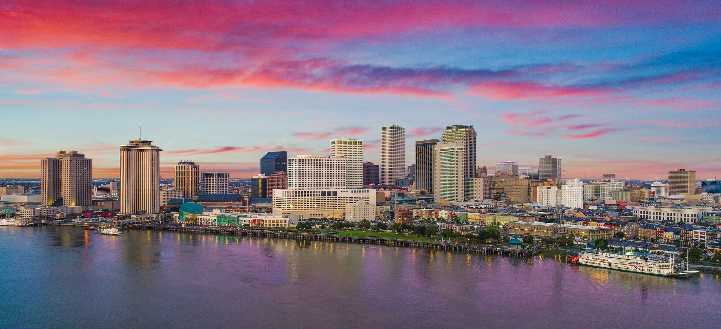 Far away shot of the New Orleans sky line along the water beneath a blue and pink sunset